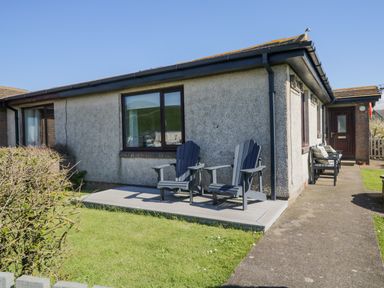 A small patio with two black chairs next to a grey house with a window and a door at Seaspray in St Bees
