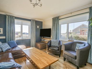 A living room with leather chairs a wooden coffee table and a wall-mounted television at Seaspray in St Bees
