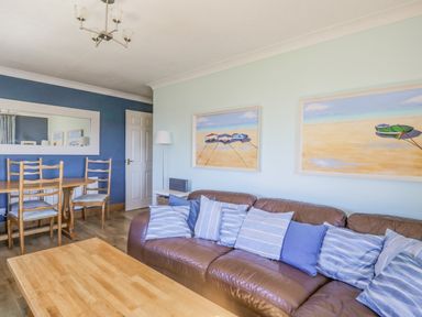 A living room with a brown leather sofa and striped cushions a wooden coffee table and dining table with chairs at Seaspray in St Bees