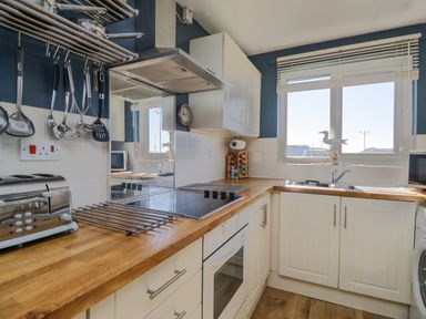 A kitchen with wooden countertops white cabinets a stove toaster hanging utensils and a window with blinds at Seaspray in St Bees