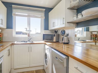 A kitchen with white cabinets wooden countertops a microwave kettle washing machine and dishwasher at Seaspray in St Bees