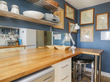 A kitchen with wooden countertops blue walls framed maps a white lamp stools and kitchen appliances at Seaspray in St Bees