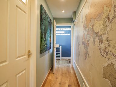 A hallway with a wooden floor and a world map on one wall and a green plant painting on the other wall at Seaspray in St Bees