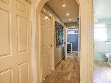 A hallway with four doors and wooden floor at Seaspray in St Bees