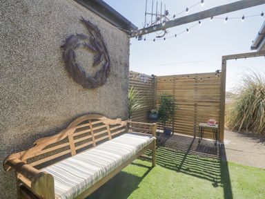An outdoor seating area with a wooden bench, potted plants, string lights, and a decorative fish wreath on the wall at Seaspray in St Bees