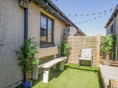An outdoor patio area with a bench, chair, potted plants, string lights, and a wooden fence at Seaspray in St Bees