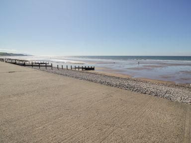 A beach with pebbles and sand next to a concrete walkway and wooden groynes at Seaspray in St Bees
