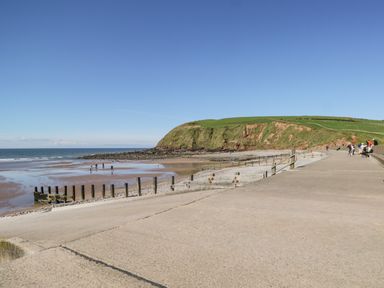 A coastal walkway with people walking near a beach and grassy cliffs at Seaspray in St Bees