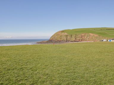 A grassy field leading to a beach and a cliff with a small building and campervan near the shore at Seaspray in St Bees