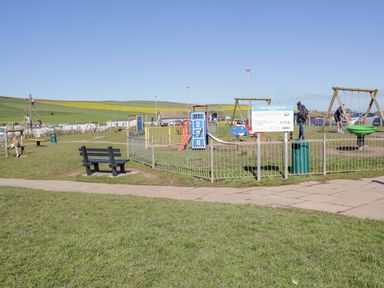 An outdoor play area with swings slides climbing structures and benches at a beach play area in St Bees