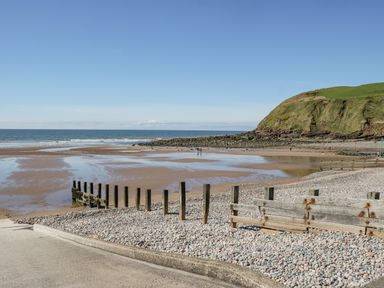 A pebble beach with wooden posts and a hill in the background at Seaspray in St Bees