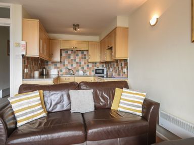 A kitchen with wooden cabinets and tiled backsplash behind a brown leather sofa with four pillows at 3 Bay View Court in Lyme Regis