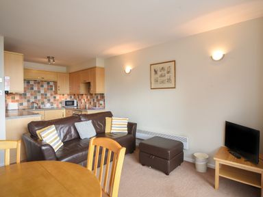 A living area with a brown leather sofa and pillows next to a kitchen with wooden cabinets and tiled backsplash at 3 Bay View Court in Lyme Regis