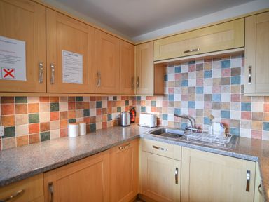 A kitchen with wooden cabinets a tiled backsplash a sink a kettle and a toaster at 3 Bay View Court Lyme Regis