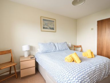 A bedroom with a bed with blue and white patterned bedding and yellow towels on it with wooden chairs and a bedside table with a lamp at 3 Bay View Court in Lyme Regis