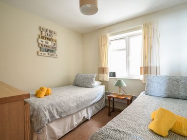 A bedroom with two single beds a wooden nightstand with a lamp and a window with curtains at 3 Bay View Court Lyme Regis