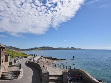 A coastal pathway with people walking near a stone wall and a beach at 3 Bay View Court in Lyme Regis
