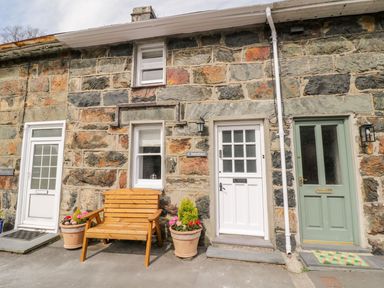 A stone exterior of a house with three doors two flower pots and a wooden bench at Henfro in Beddgelert