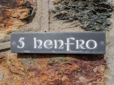 A house number plaque reading 5 henfro mounted on a stone wall at Henfro in Beddgelert