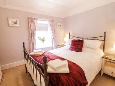 A bedroom with a metal bed frame white bedding red throws and towels on the bed floral curtains and bedside tables with lamps at Henfro in Beddgelert