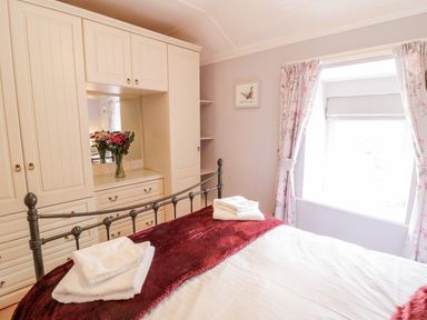 A bedroom with a metal bed frame towels on the bed built-in wardrobes and a window with floral curtains at Henfro in Beddgelert