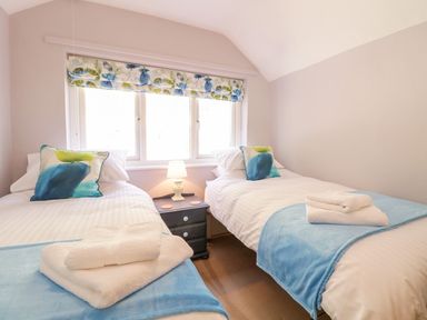 A bedroom with two single beds blue blankets on the beds a nightstand with a lamp between the beds and a window with floral blinds at Henfro in Beddgelert