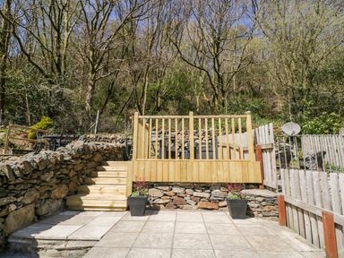 A tiered stone and wooden fenced garden with steps and potted plants at Henfro in Beddgelert
