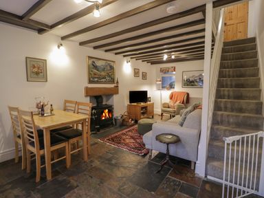 A living room with a dining table with four chairs a wood burning stove a TV an armchair a sofa a carpet and stairs with a baby gate at Henfro in Beddgelert