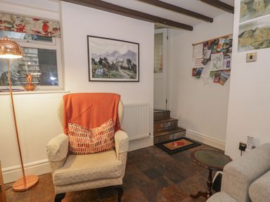 An armchair with an orange throw and pillow next to a floor lamp and window in a room with stairs and a bulletin board at Henfro in Beddgelert