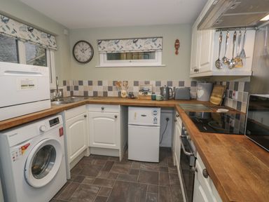 A kitchen with white cabinets wooden countertops a washing machine a small refrigerator and cooking utensils at Henfro in Beddgelert