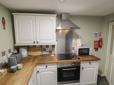 A kitchen with white cabinets wooden countertops a stove microwave toaster kettle and fire safety equipment at Henfro in Beddgelert