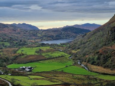 A valley with green fields a farm lake and hills in the background at Henfro in Beddgelert