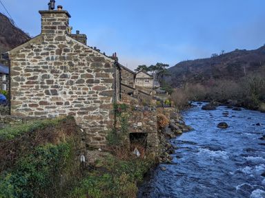 Stone houses beside a flowing river with hills in the background at Henfro in Beddgelert