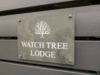 A sign with a tree illustration and text watch tree lodge on a wooden surface at Watch Tree Lodge in Allithwaite near Cartmel