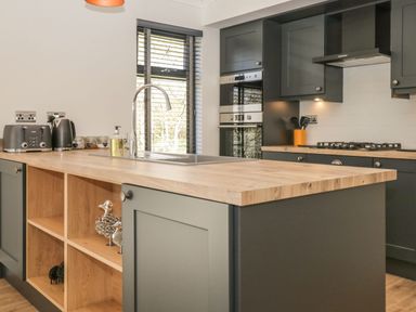 A kitchen with wooden countertop black cabinets a toaster kettle sink and gas stove at Watch Tree Lodge in Allithwaite near Cartmel