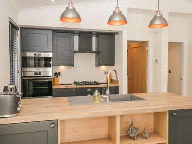 A kitchen with dark cabinets wooden countertops a sink three hanging lights and built in oven at Watch Tree Lodge in Allithwaite near Cartmel