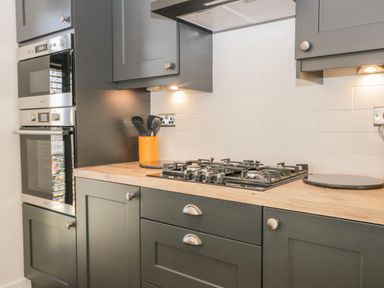 A kitchen with a gas stove oven built into dark cabinets and wooden countertop at Watch Tree Lodge Allithwaite near Cartmel