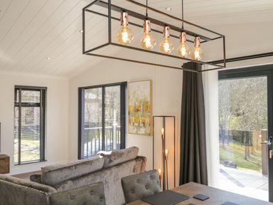 A living room with gray sofas a wooden table modern lighting large windows and a painting at Watch Tree Lodge in Allithwaite near Cartmel