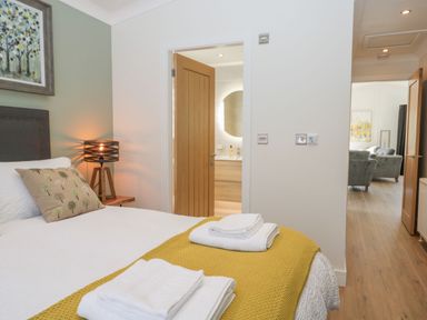 A bedroom with a bed a lamp an open door showing a bathroom and another open door revealing a living room at Watch Tree Lodge Allithwaite near Cartmel