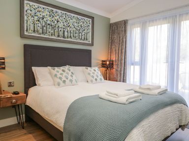 A bedroom with a large bed with white linens and a blue throw at Watch Tree Lodge in Allithwaite near Cartmel