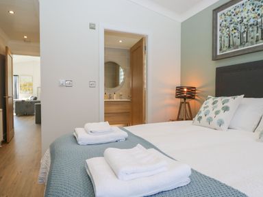 A bedroom with a bed with folded towels a bedside lamp and a door leading to a bathroom at Watch Tree Lodge in Allithwaite near Cartmel