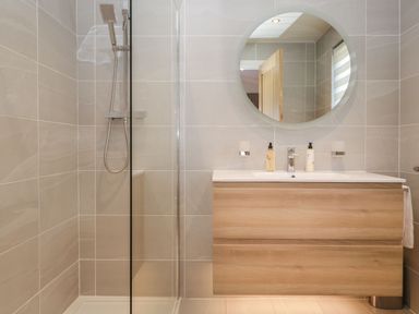 A bathroom with a shower enclosure and a wooden vanity unit with a round mirror at Watch Tree Lodge in Allithwaite near Cartmel