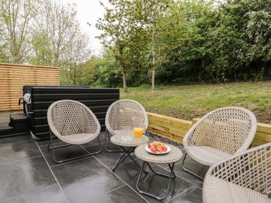 An outdoor patio with wicker chairs a hot tub and a table with orange juice and croissants at Watch Tree Lodge in Allithwaite near Cartmel