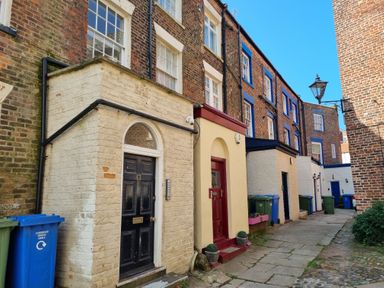 A narrow alley with several brick buildings featuring doors and recycling bins at The Seahome in Scarborough