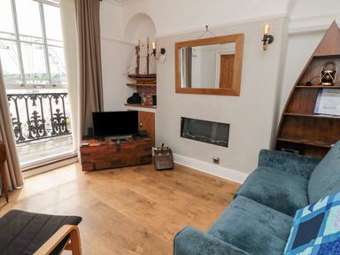 A living room with a television on a wooden chest a blue sofa and a triangular wooden shelf at The Seahome in Scarborough