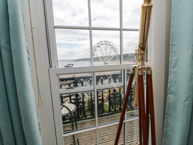 A telescope on a tripod in front of a window with a view of a Ferris wheel and beach at The Seahome in Scarborough
