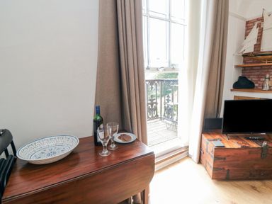 A room with a wooden table holding a bottle of wine two glasses and a plate of biscuits near a window with curtains and a wooden chest with a television at The Seahome in Scarborough