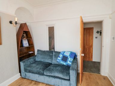 A room with a blue sofa a wooden boat-shaped bookshelf and an open wooden door at The Seahome in Scarborough