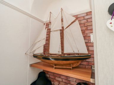 A model sailboat with cream sails on a wooden shelf against a brick wall at The Seahome in Scarborough
