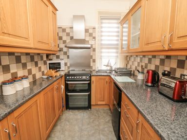 A kitchen with wooden cabinets a stove a microwave a sink and red kettle at The Seahome in Scarborough